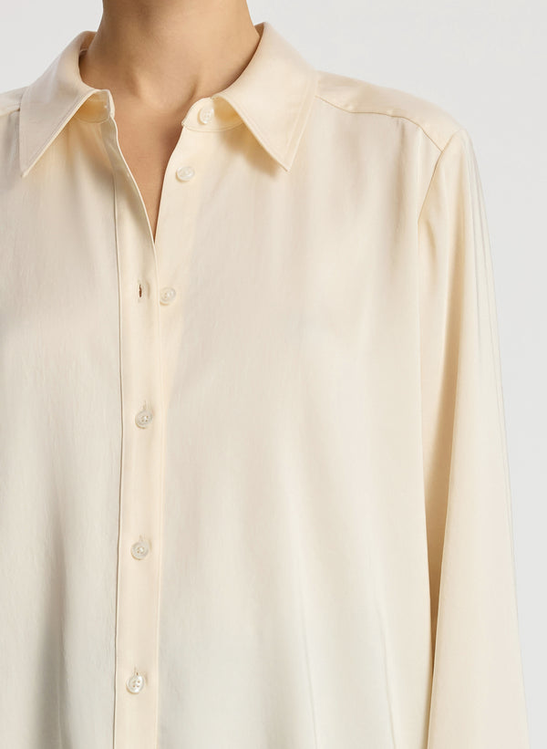 detail view of woman wearing cream long sleeve button down collared shirt and dark wash denim jeans