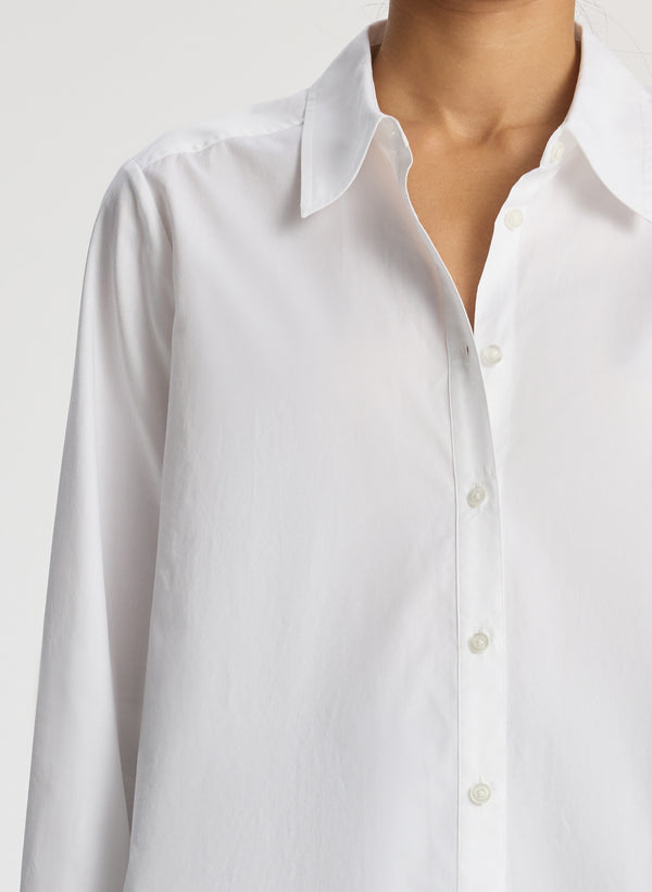 detail view of woman wearing white button down collared shirt and dark wash wide leg raw denim jeans