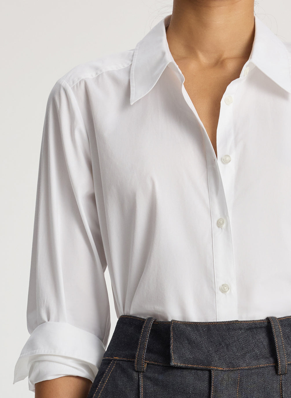 detail view of woman wearing white button down collared shirt and dark wash wide leg raw denim jeans