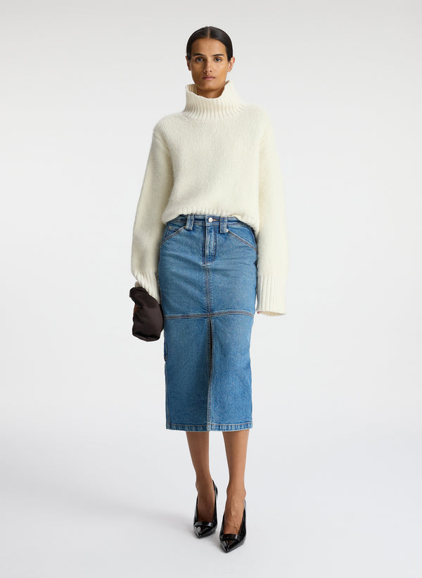 front view of woman wearing ivory sweater and medium blue wash denim midi skirt