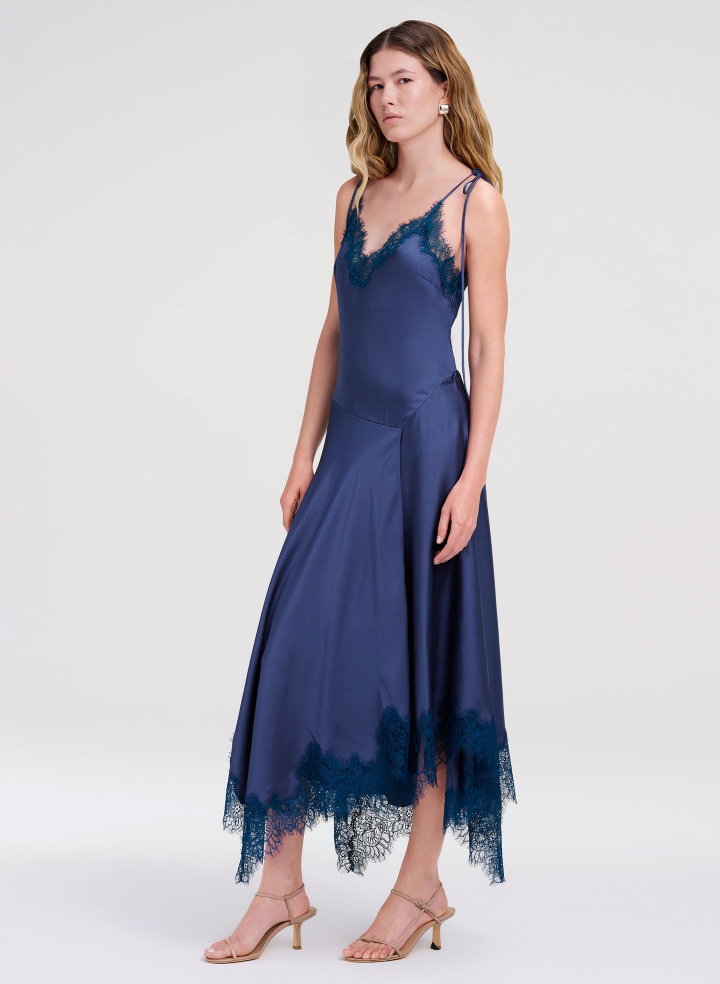 Woman wearing a navy blue slip dress with lace details on a white background
