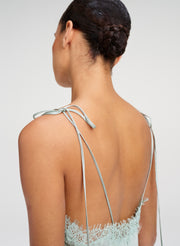 Rear view of a woman wearing a pale blue lace dress with thin tie-back straps, shown against a light gray studio background.