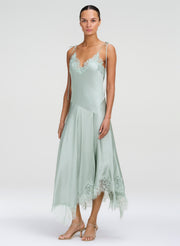 A model wearing a sage green satin slip dress with lace trim on a light gray studio background.