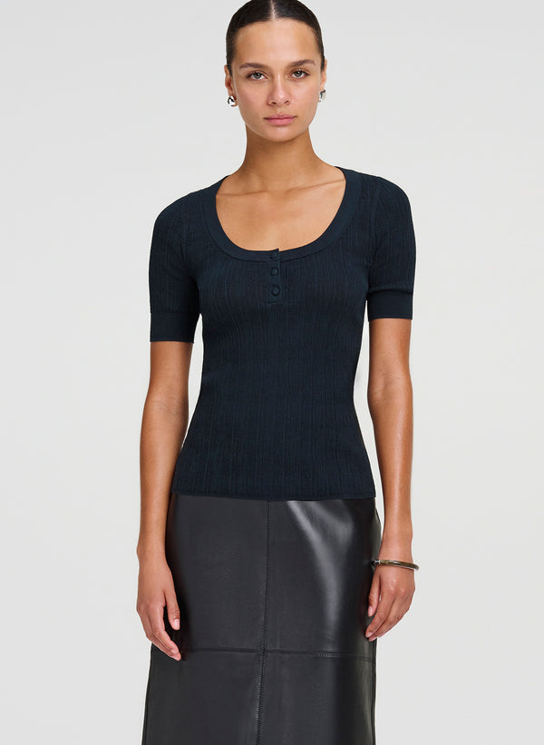 Woman wearing a dark green short-sleeve top and black skirt on a light gray background
