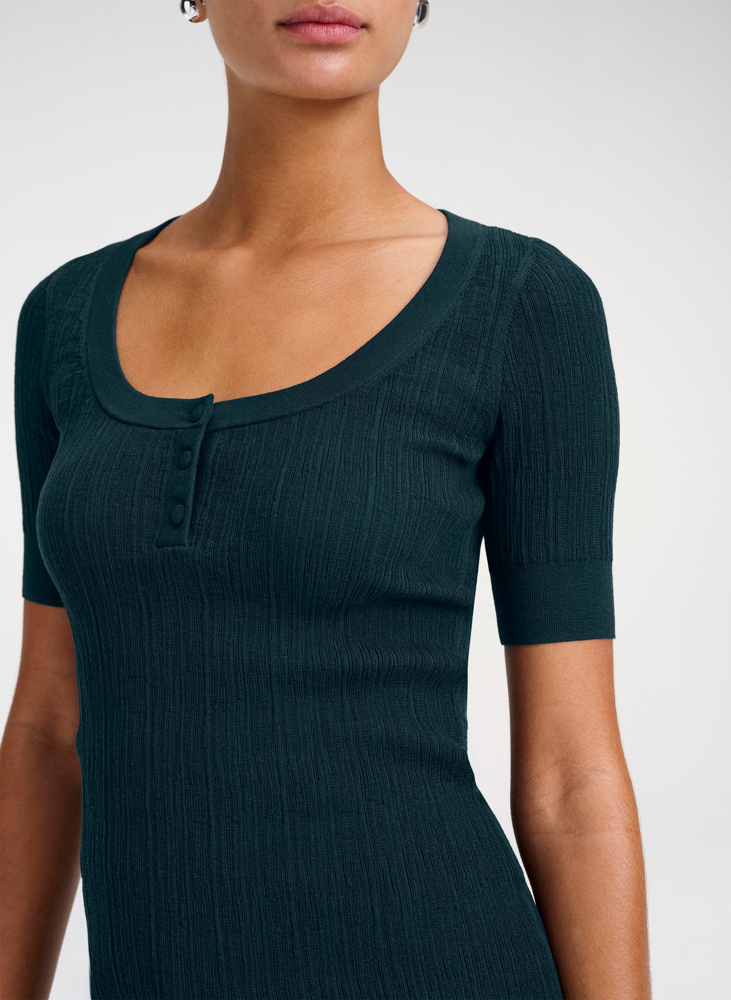 A close-up of a woman wearing a dark teal ribbed short-sleeve henley top with a scoop neckline and three buttons.