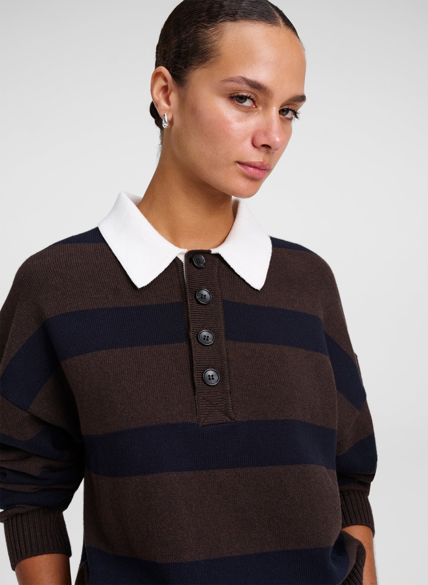 A close-up of a woman wearing a brown and navy blue horizontally striped knit polo sweater with a contrasting white collar.