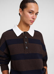 A close-up of a woman wearing a brown and navy blue horizontally striped knit polo sweater with a contrasting white collar.