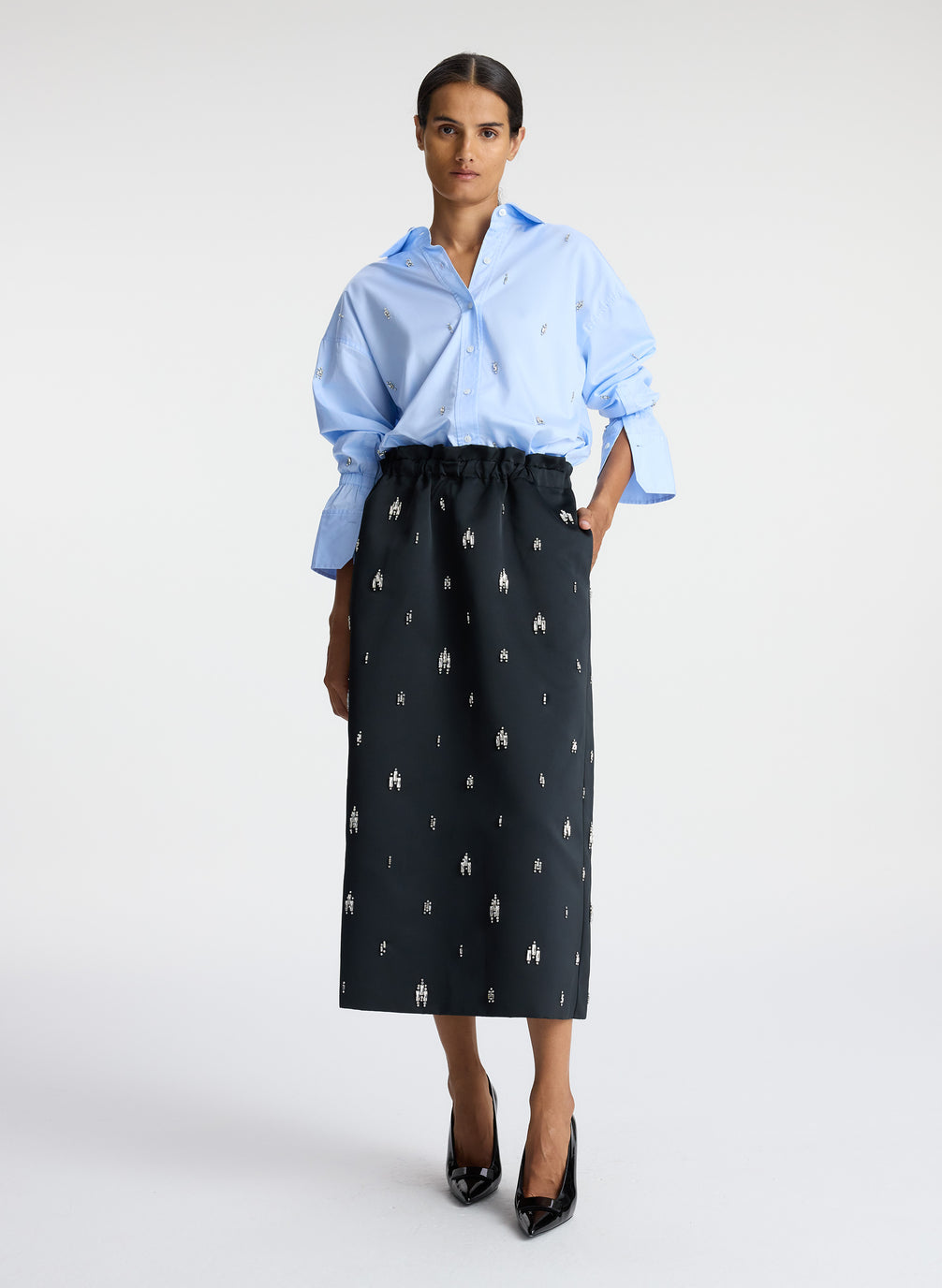 front view of woman wearing blue embellished button down top and black embellished midi skirt