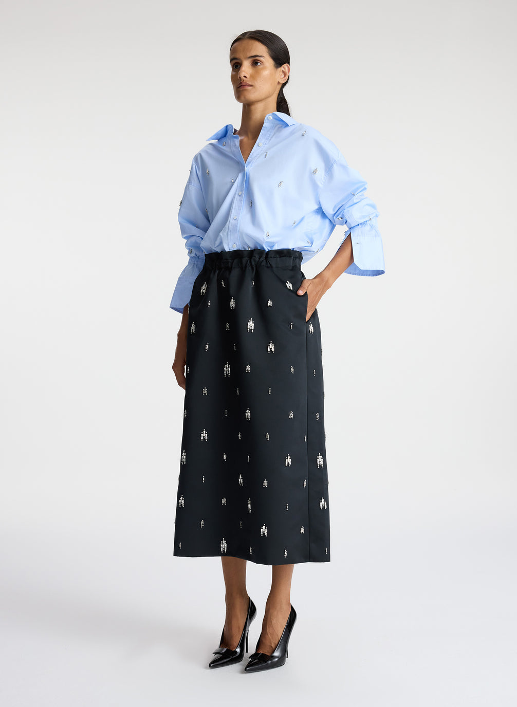 side view of woman wearing blue embellished button down top and black embellished midi skirt