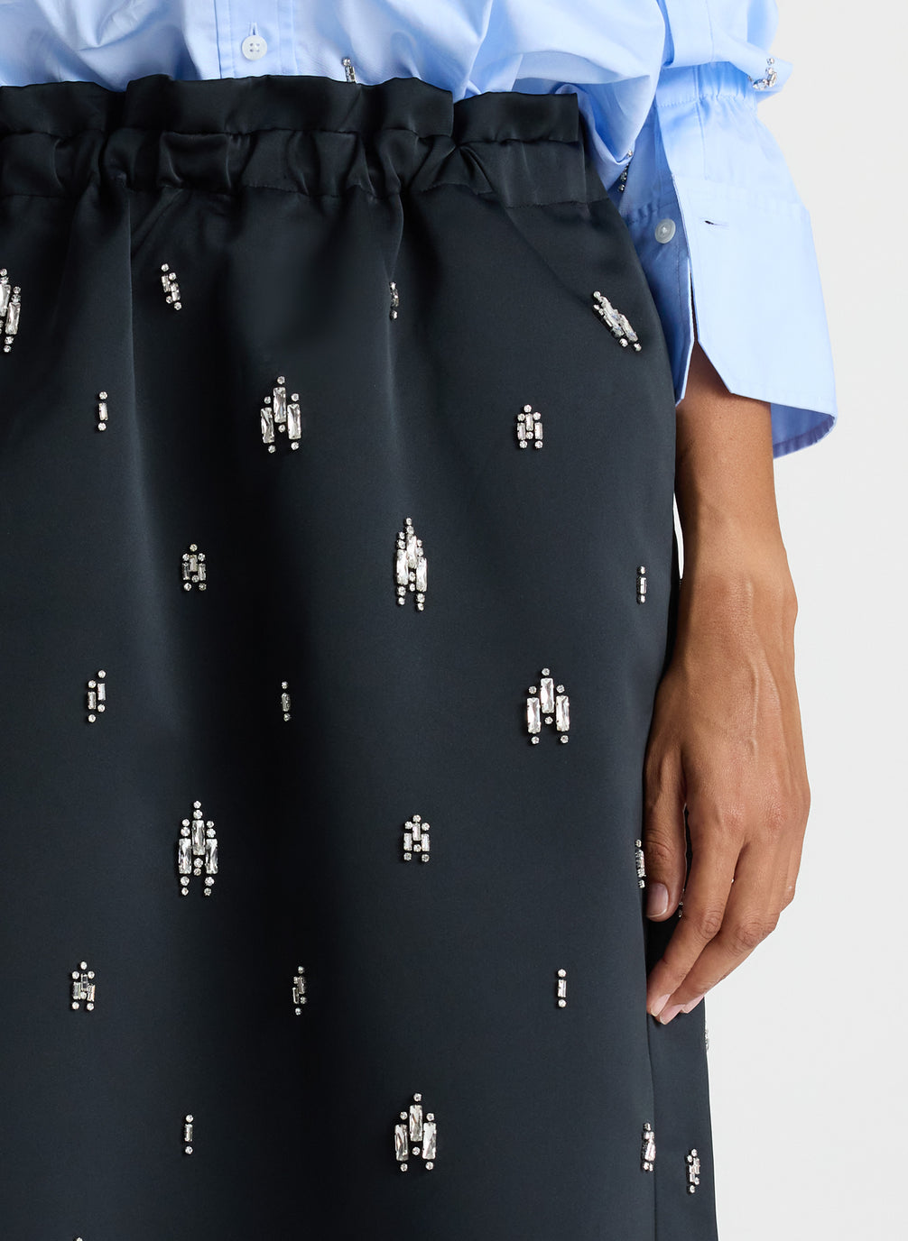 detail view of woman wearing blue embellished button down top and black embellished midi skirt