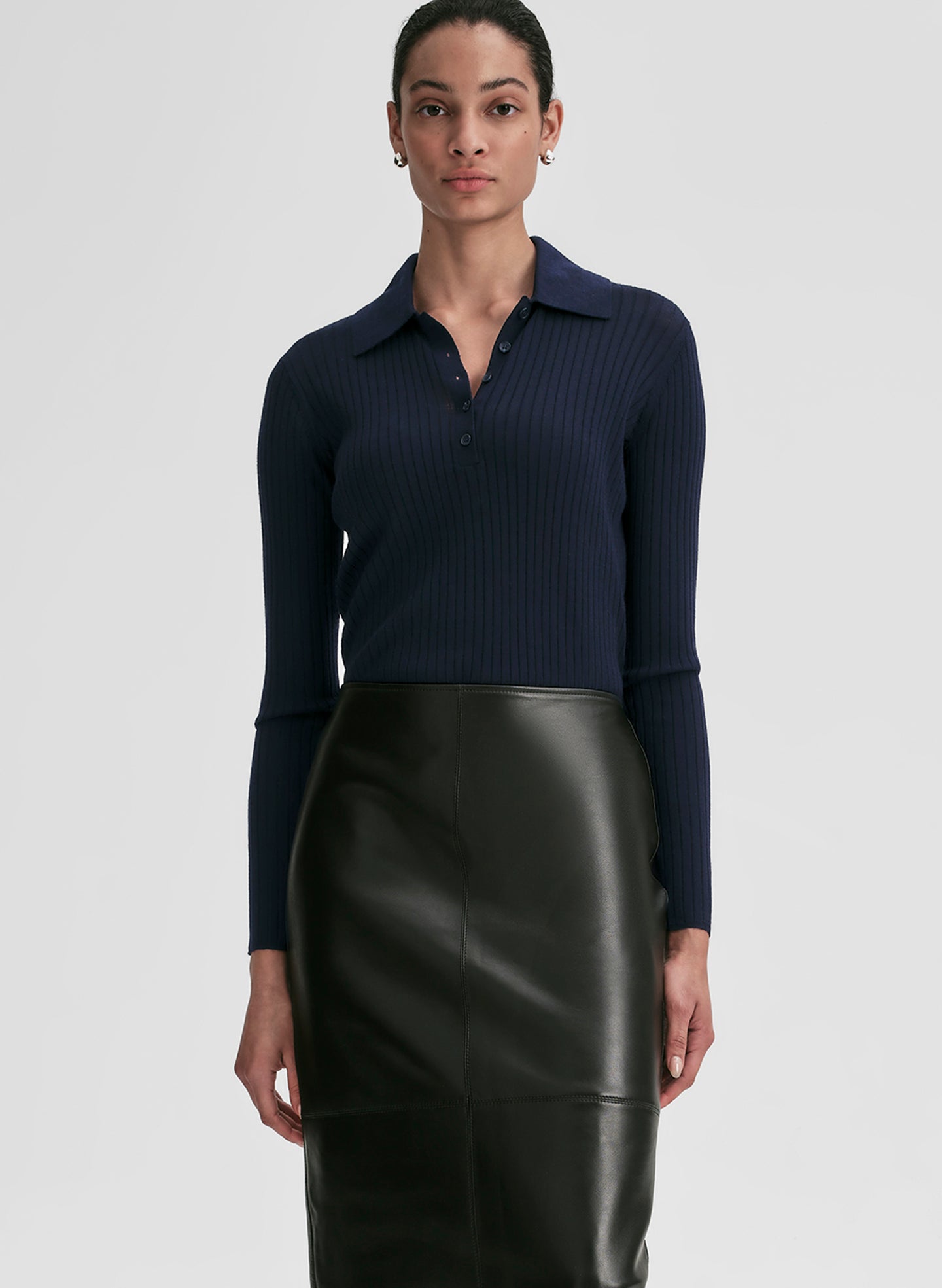 Woman wearing a navy ribbed long-sleeve shirt and black leather skirt on a light gray background