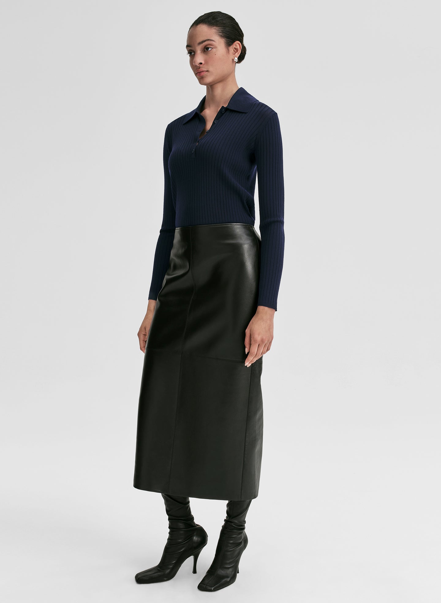 Woman wearing a navy ribbed long-sleeve shirt and black leather skirt on a light gray background