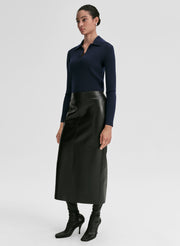 Woman wearing a navy ribbed long-sleeve shirt and black leather skirt on a light gray background