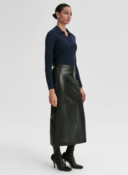 Woman wearing a navy ribbed long-sleeve shirt and black leather skirt on a light gray background