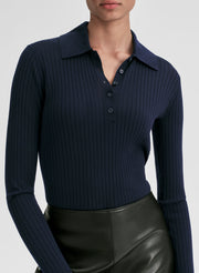 Woman wearing a navy ribbed long-sleeve shirt and black leather skirt on a light gray background