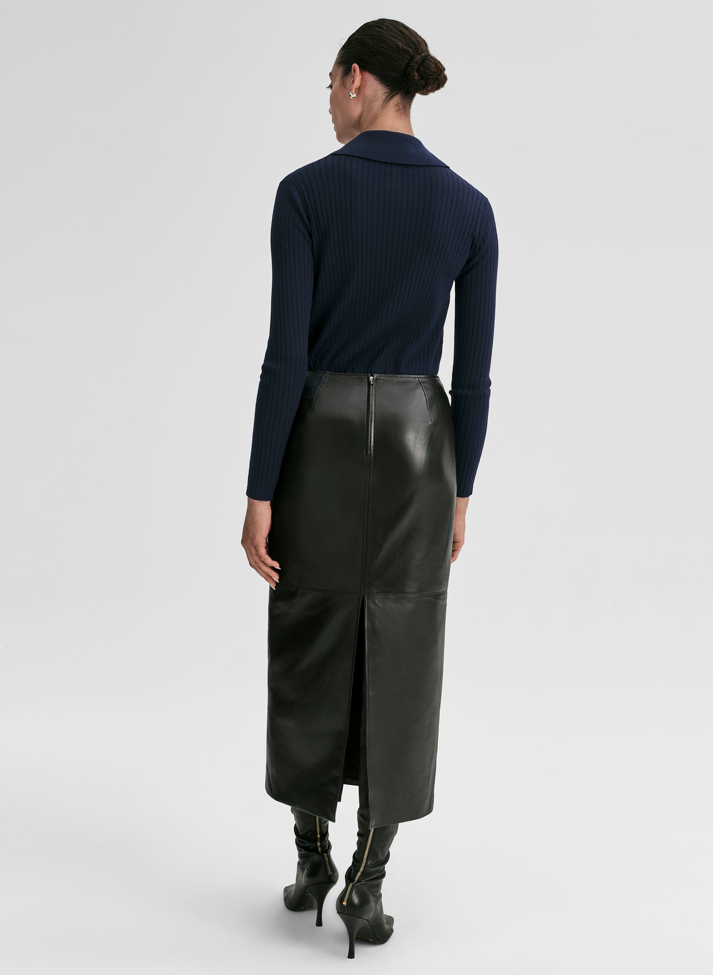 Woman wearing a navy ribbed long-sleeve shirt and black leather skirt on a light gray background