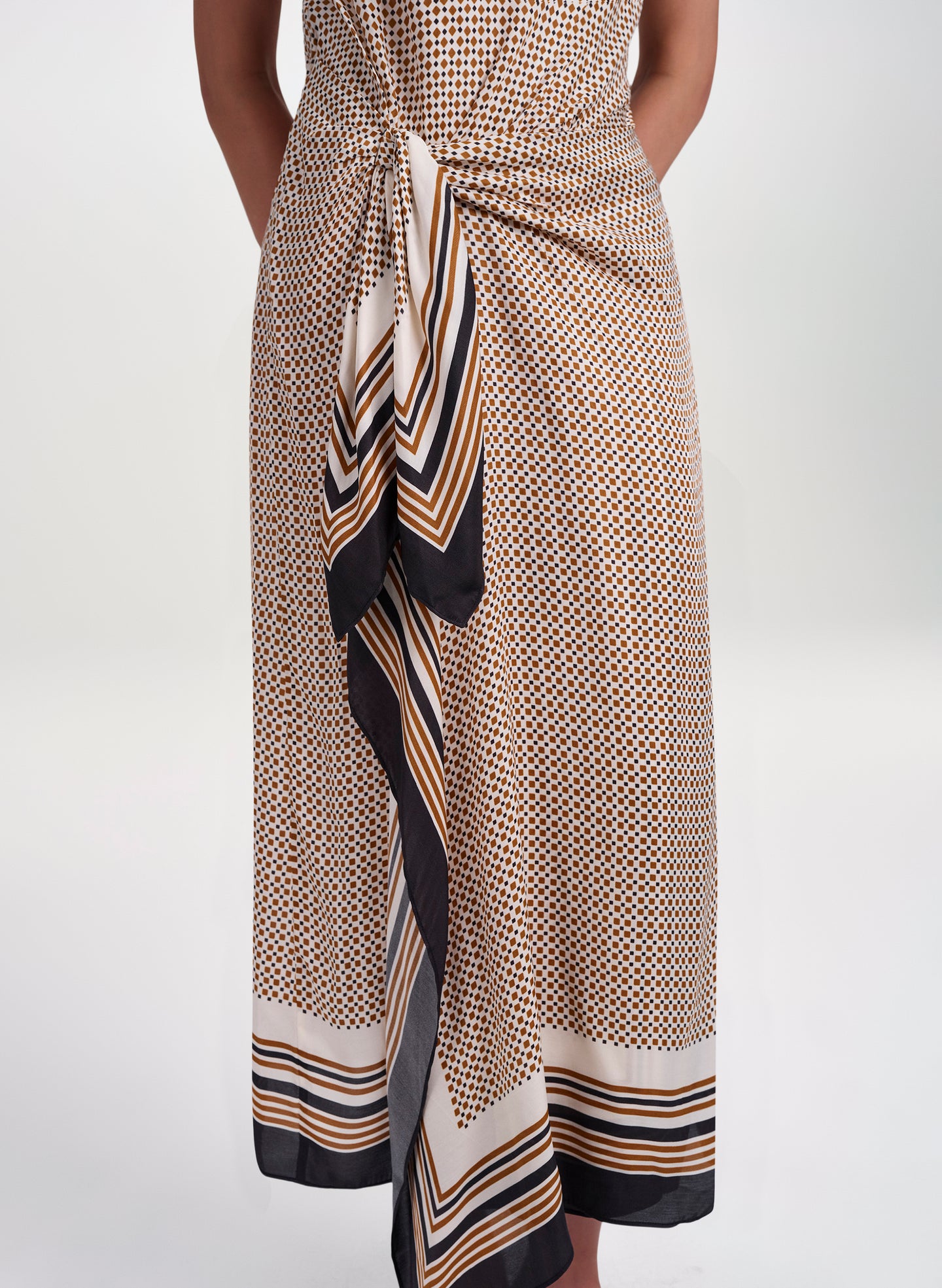 A close-up of a model wearing a wrap-style midi dress with a beige, black, and orange geometric pattern and striped tie detail.