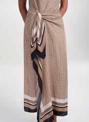 A close-up of a model wearing a wrap-style midi dress with a beige, black, and orange geometric pattern and striped tie detail.