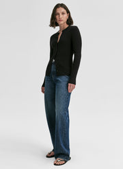 Woman wearing a black long-sleeve cardigan and blue jeans on a white background