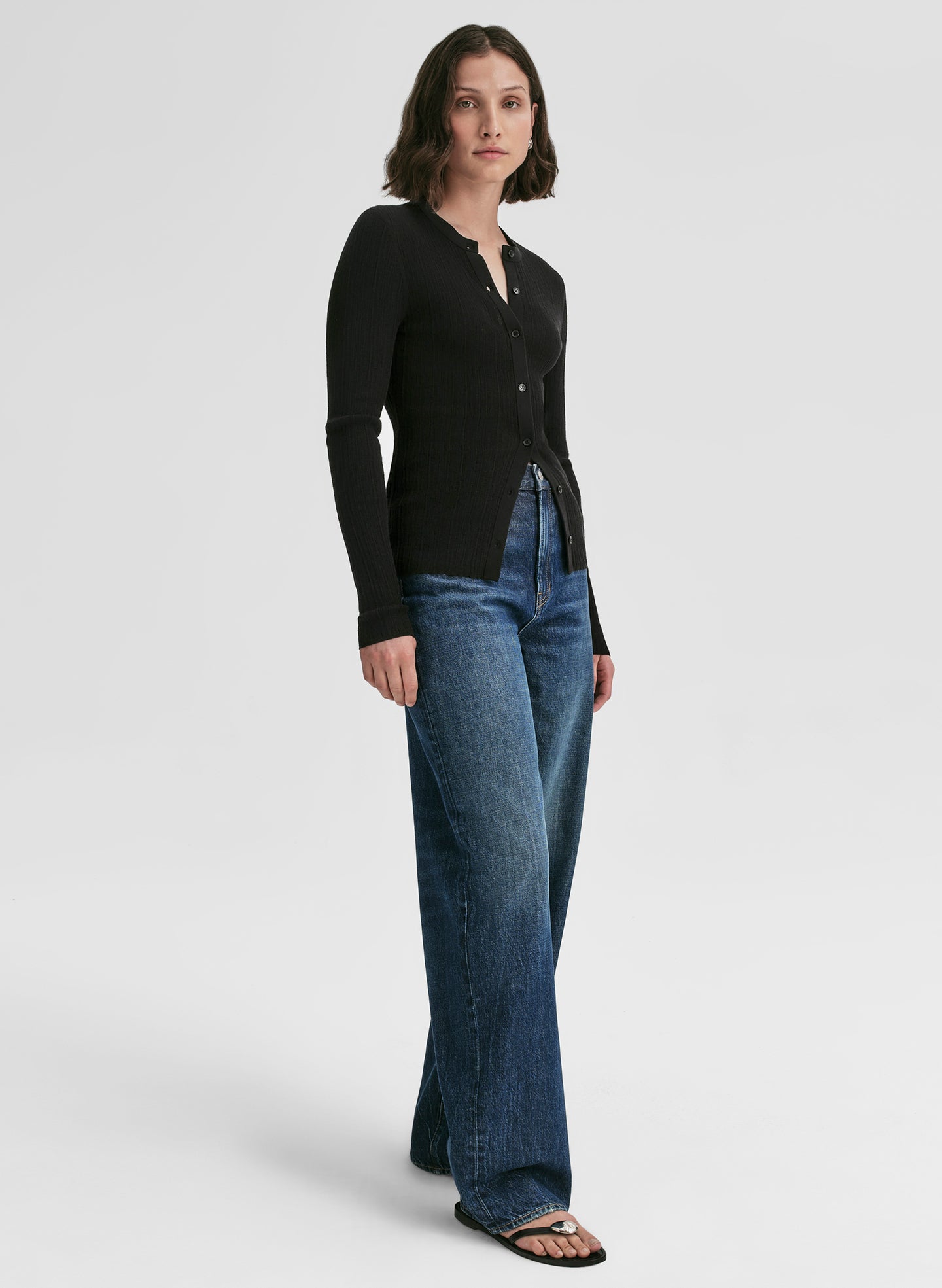 Woman wearing a black long-sleeve cardigan and blue jeans on a white background