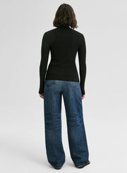 Woman wearing a black long-sleeve cardigan and blue jeans on a white background