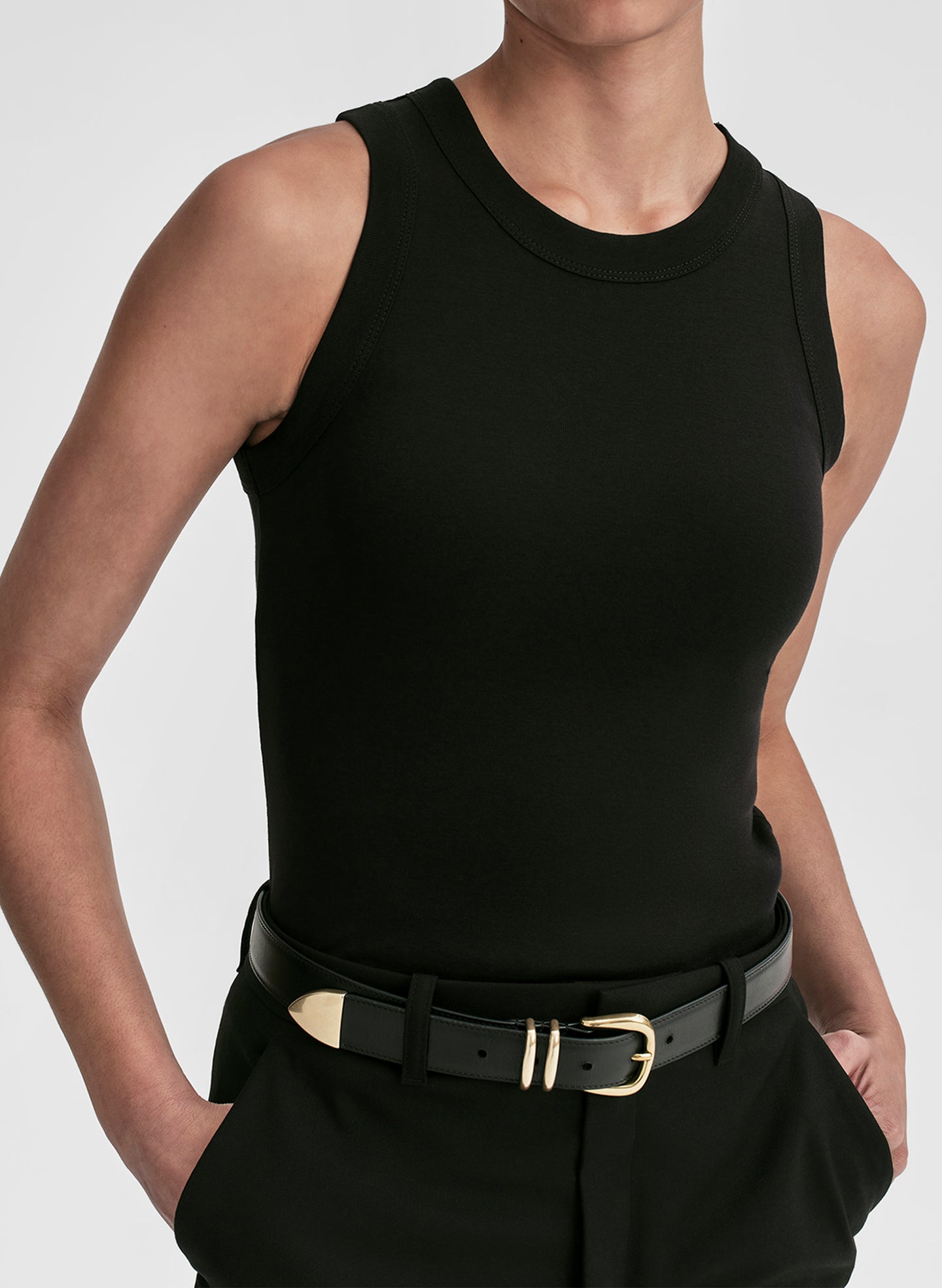 Person wearing a black sleeveless top and black pants with a belt on a light gray background