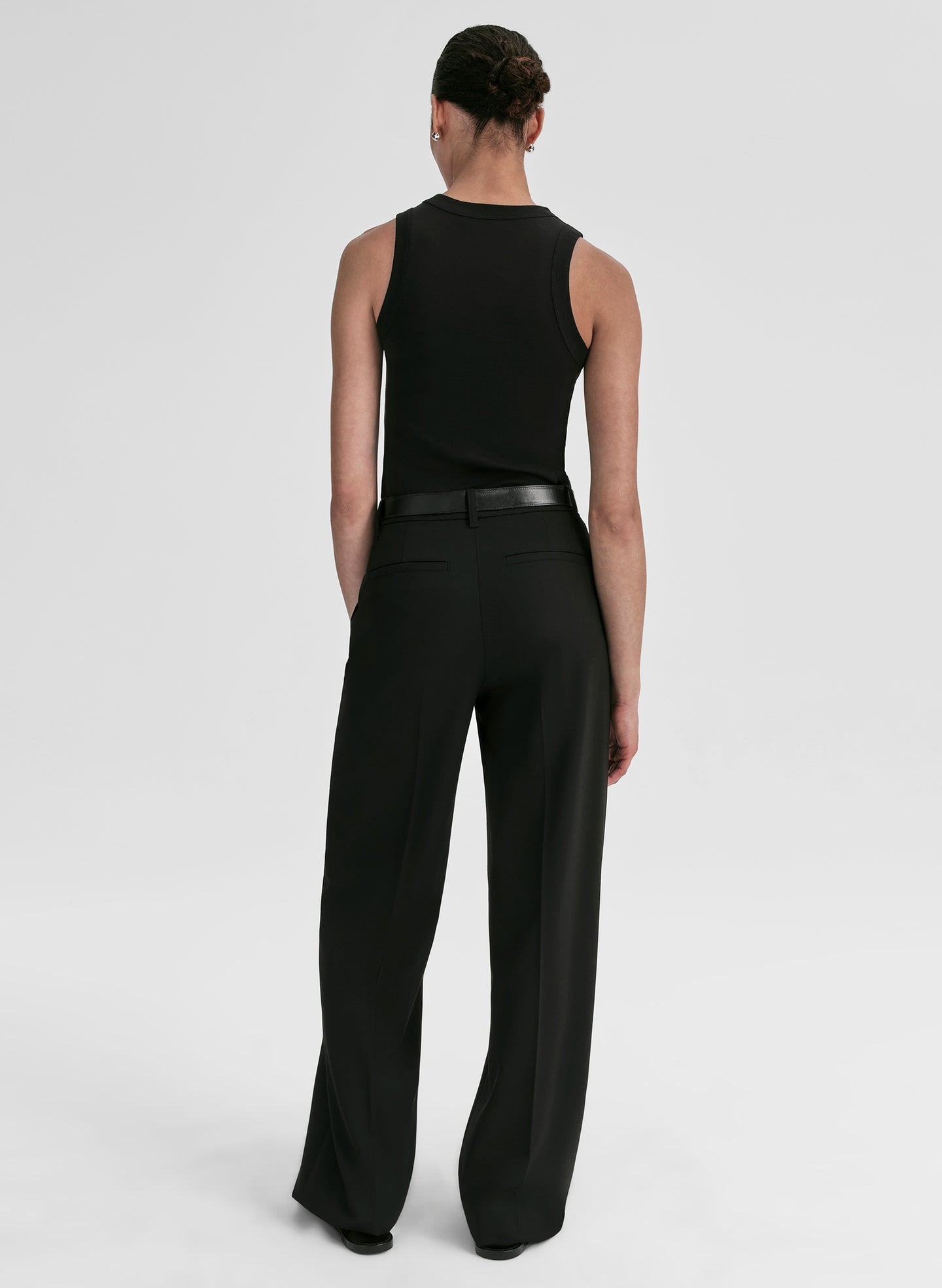 Person wearing a black sleeveless top and black pants with a belt on a light gray background