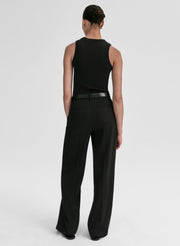 Person wearing a black sleeveless top and black pants with a belt on a light gray background