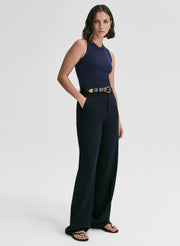 Woman wearing a navy sleeveless top and pants with a gold belt on a white background
