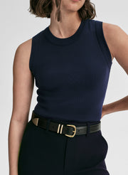 Woman wearing a navy sleeveless top and pants with a gold belt on a white background