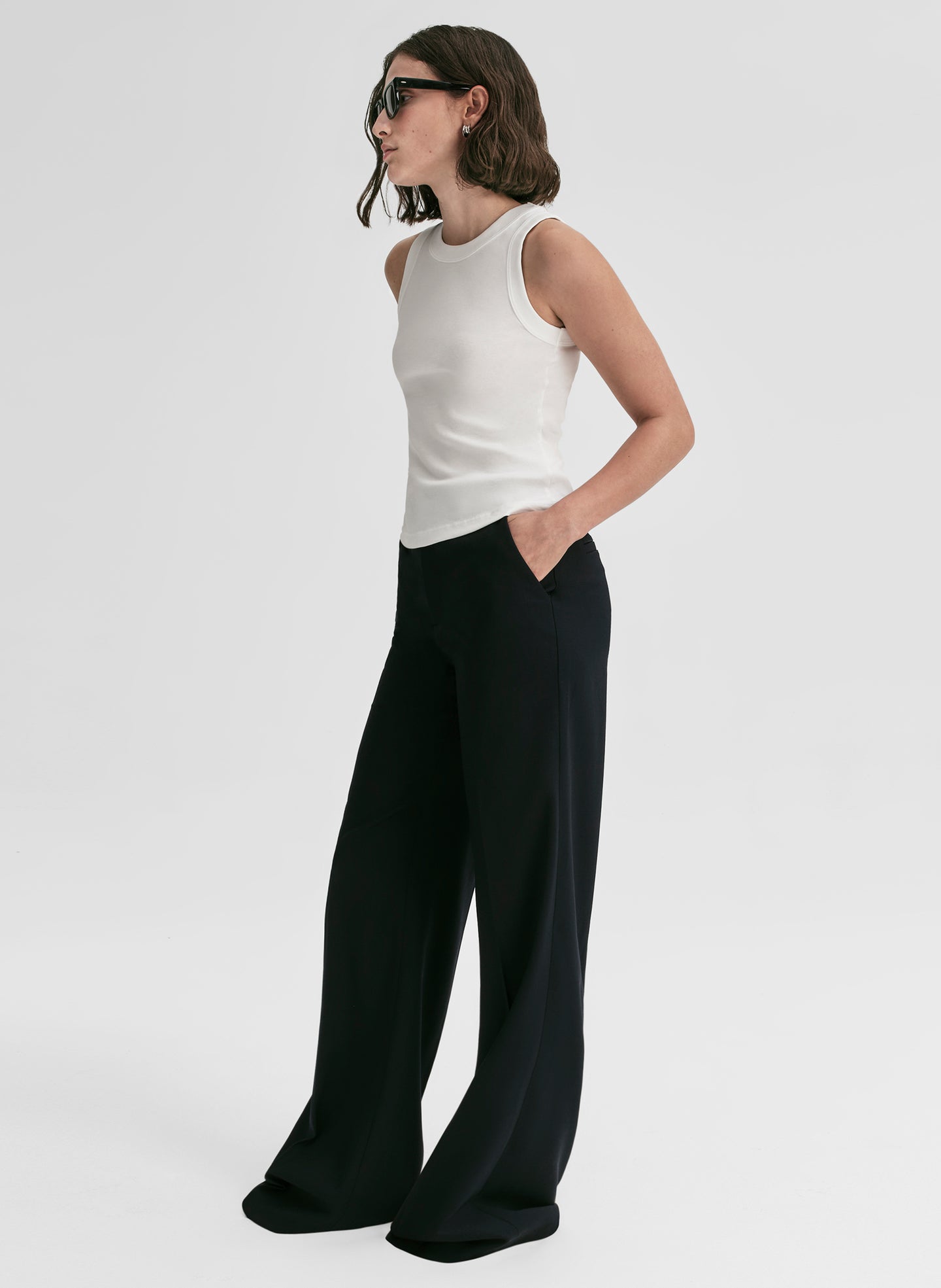 Woman wearing a white sleeveless top and black wide-leg pants on a light gray background
