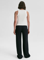 Person wearing a white sleeveless top and black pants on a white background