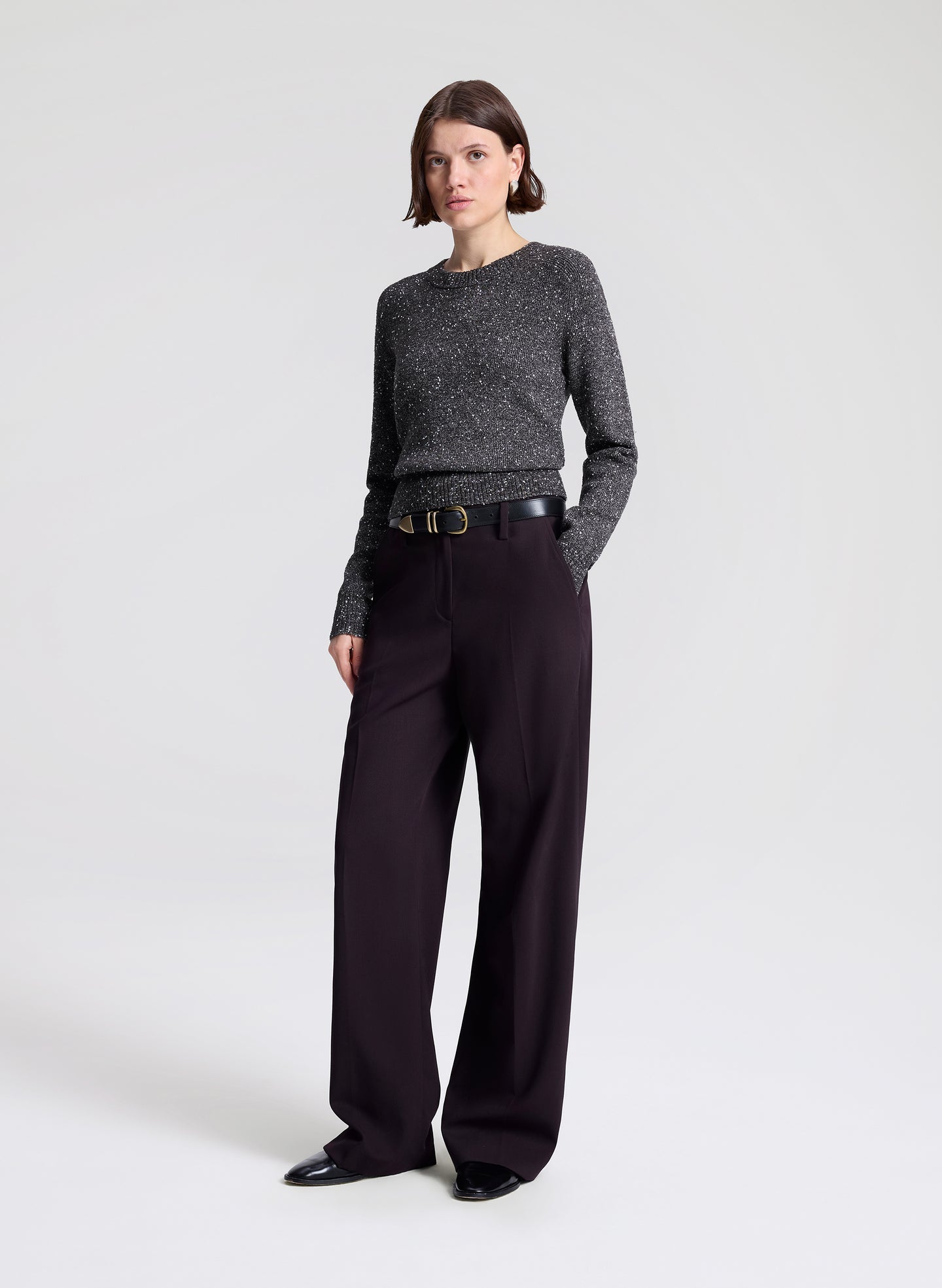 Woman wearing a gray speckled sweater and purple pants on a light gray background