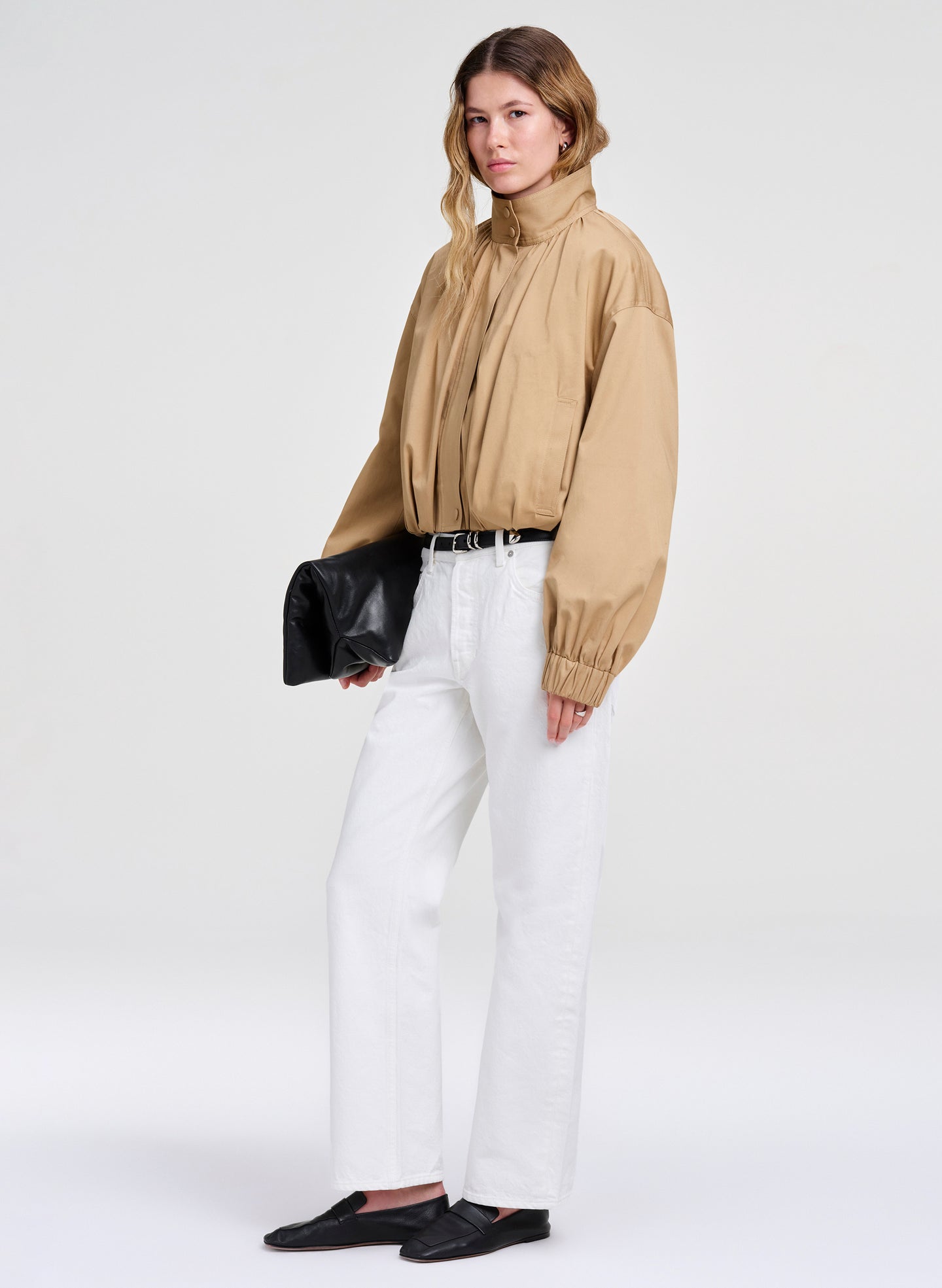 Woman wearing a beige jacket, white pants, and black shoes on a white background
