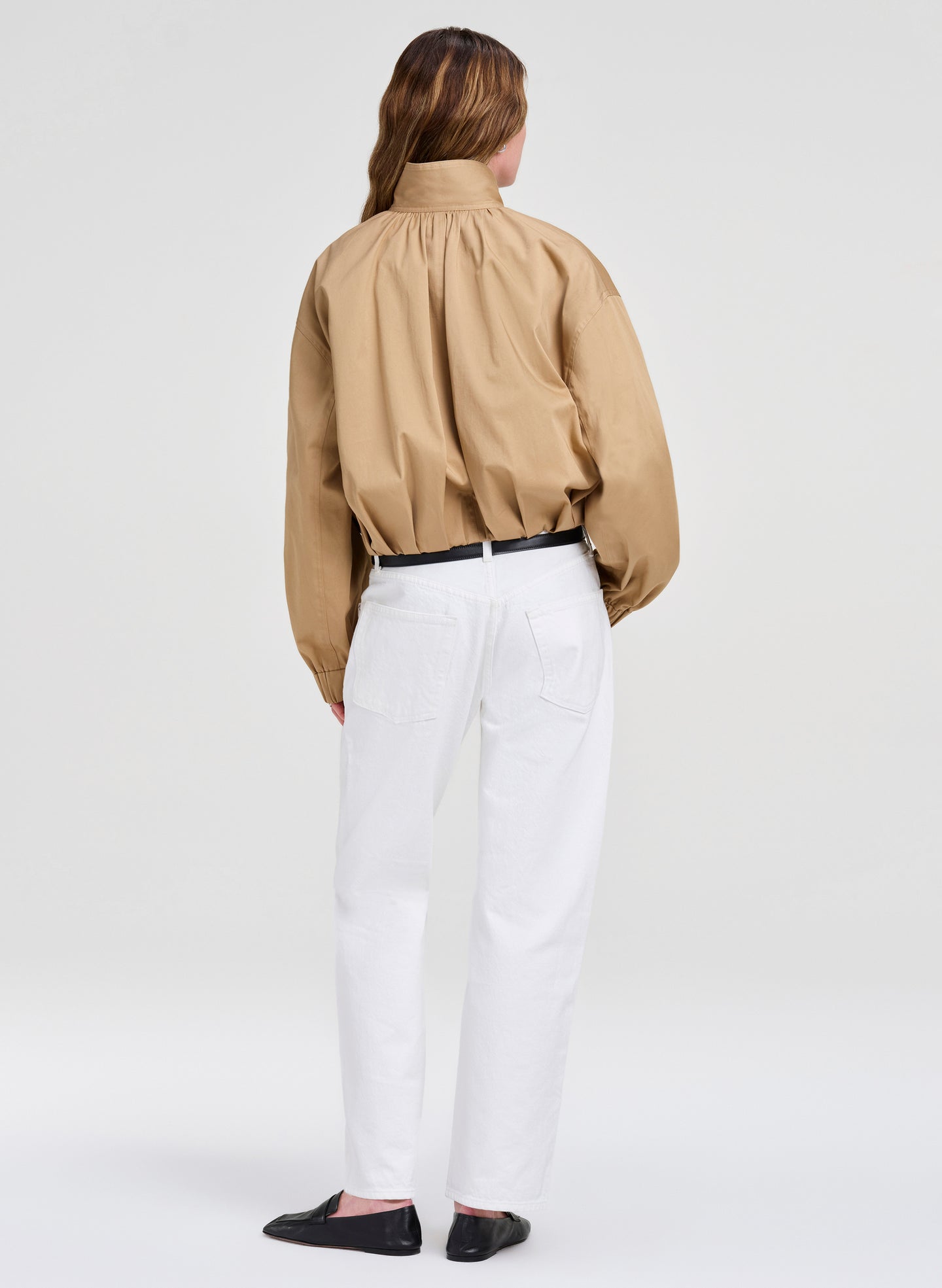 Person wearing a beige jacket and white pants on a plain background