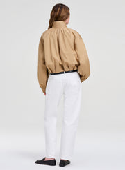 Person wearing a beige jacket and white pants on a plain background