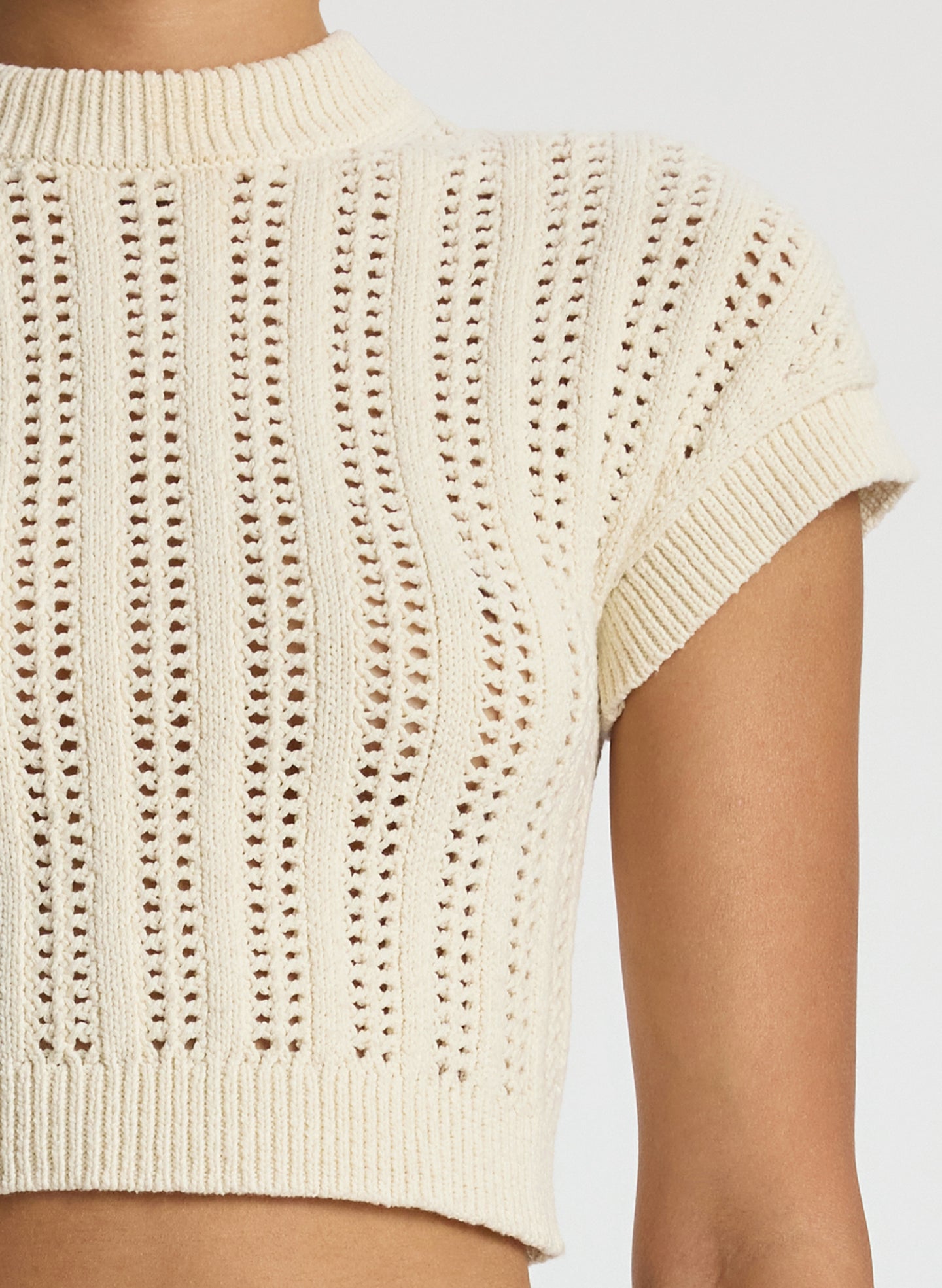detail view of woman wearing ivory short sleeve open weave top and beige wide leg pants