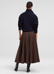 A model shown from the back wearing a dark navy mock-neck knit sweater and a brown A-line midi skirt, paired with black  boots, against a light gray studio background.