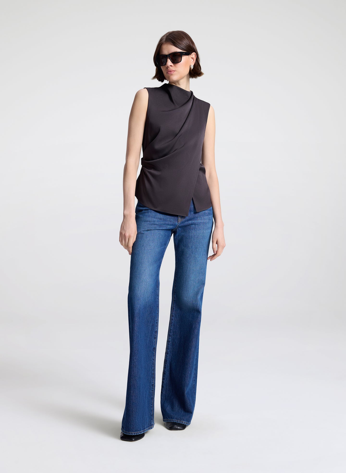 Person wearing a brown sleeveless top and blue jeans on a white background