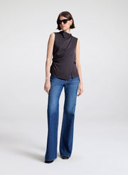 Person wearing a brown sleeveless top and blue jeans on a white background