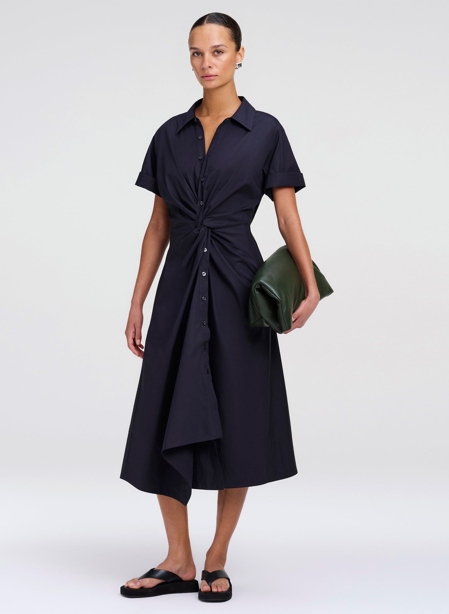 Woman wearing a navy blue dress holding a green clutch against a white background