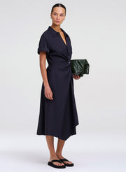 Woman wearing a dark blue dress holding a green clutch against a white background