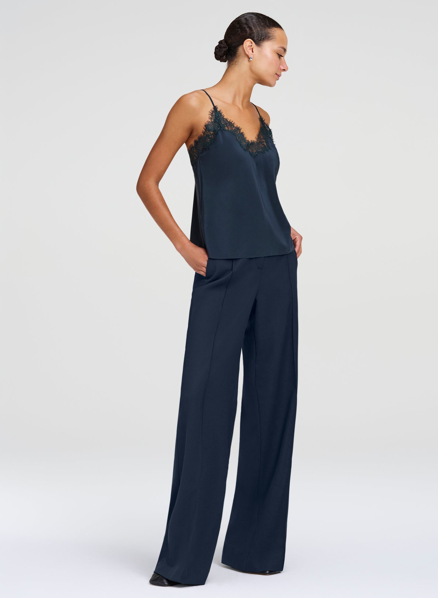 A woman modeling a green camisole top and matching pants with a lace-trimmed camisole top and wide-leg pants, photographed against a light gray studio background.