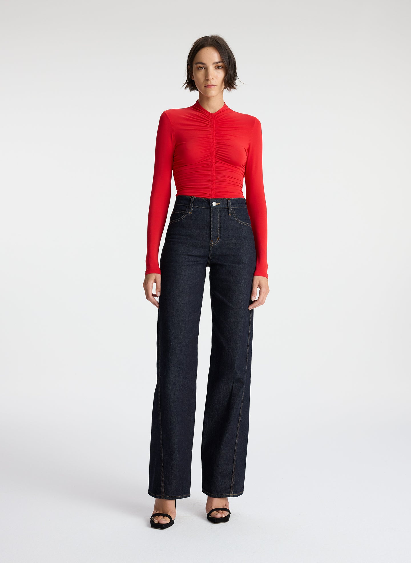 front view of woman wearing red ruched long sleeve top and dark wash jeans