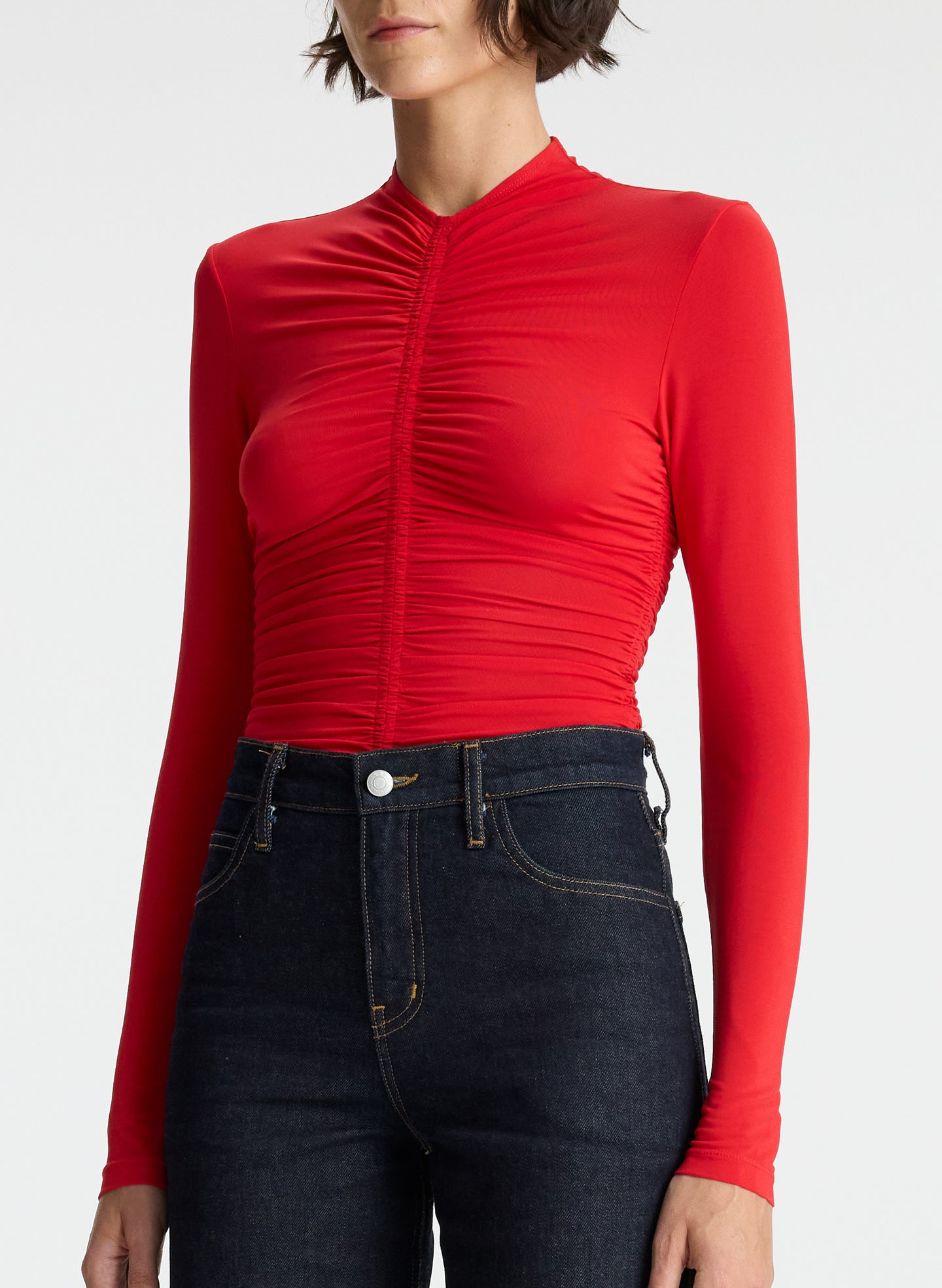 detail view of woman wearing red ruched long sleeve top and dark wash jeans