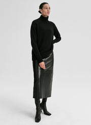Person wearing a black turtleneck sweater and leather skirt on a white background