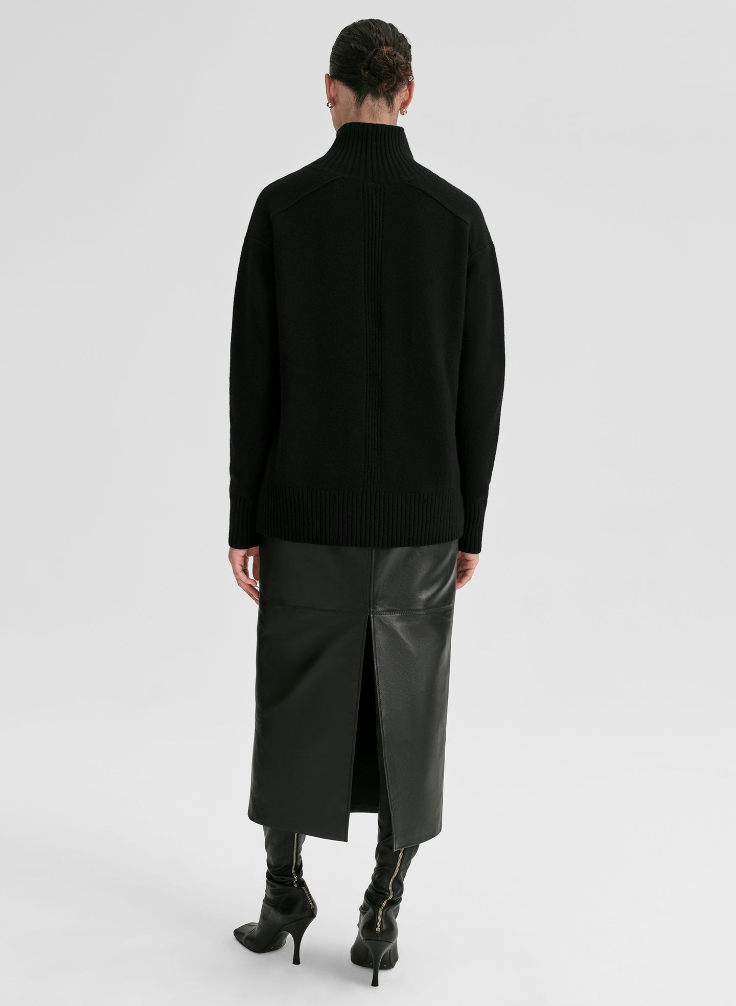 Person wearing a black turtleneck sweater and black leather skirt on a white background
