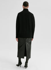Person wearing a black turtleneck sweater and black leather skirt on a white background