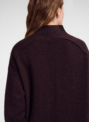 A close-up back view of a woman wearing a dark brown ribbed knit sweater against a light gray studio background.