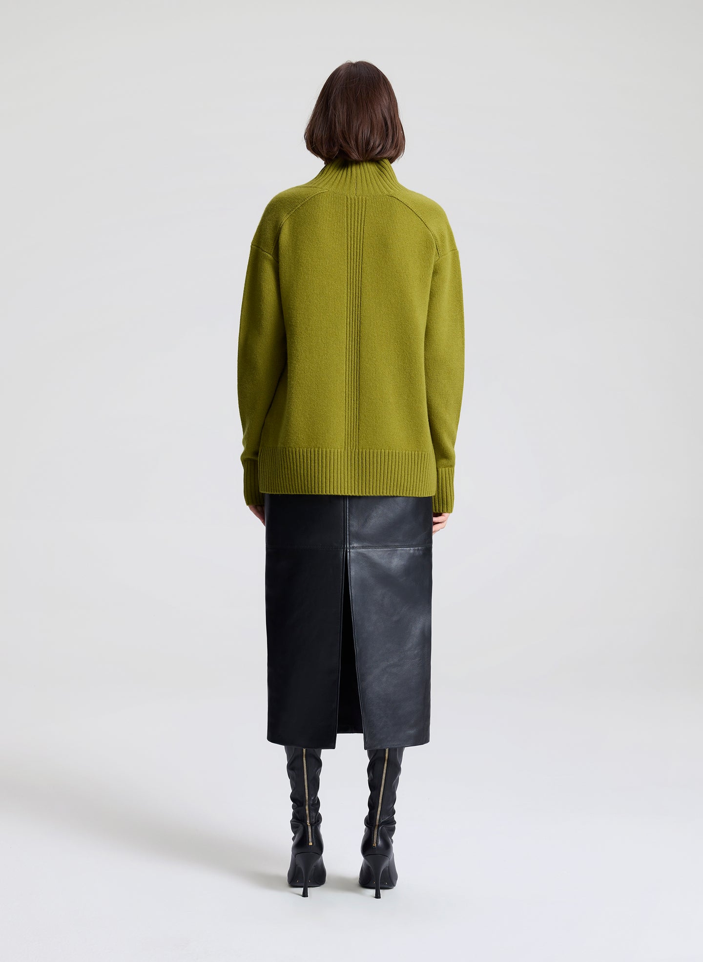 Woman wearing a green sweater and black leather skirt against a white background